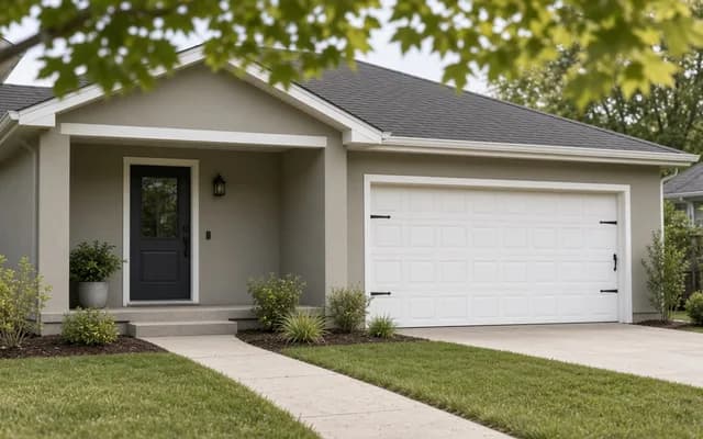 Freshly painted grey stucco bungalow with a white paneled garage door, black front door and a curving path through lawn