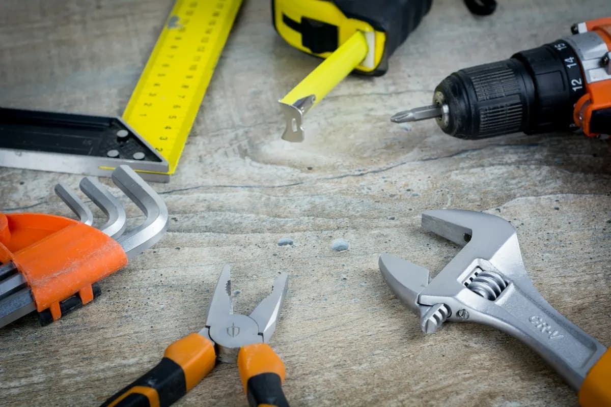 Tape measure, cordless drill and adjustable spanners on a workbench
